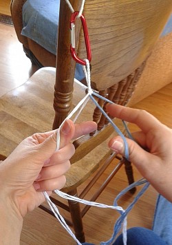 Each hand holds two separate strings or two separate groups of strings.  Here one side is blue and the other white.