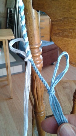 After plaiting 13, secure the blue strings with a knot and plait the remaining white strings 13 times